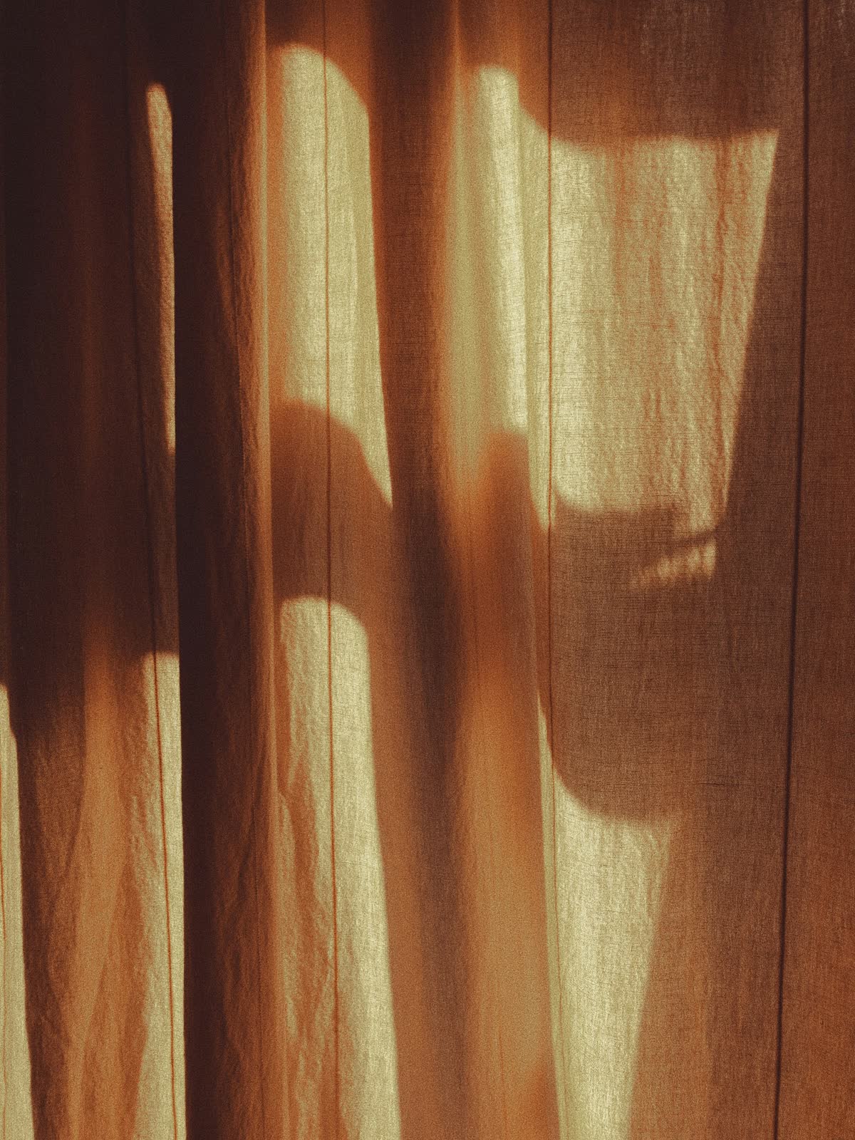 Warmes Licht fällt durch einen Vorhang und zeichnet ein Schattenmuster auf den Stoff